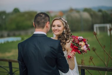 Gelin ve damat bir tarlada, gelin bir buket çiçek tutuyor. Sahne mutlu ve kutlama dolu, çünkü çift evleniyor.
