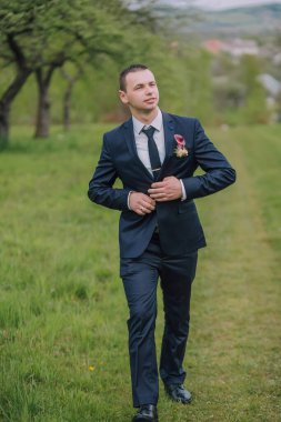 Takım elbiseli ve kravatlı bir adam tarlada yürüyor. Elinde kırmızı bir çiçek tutuyor.