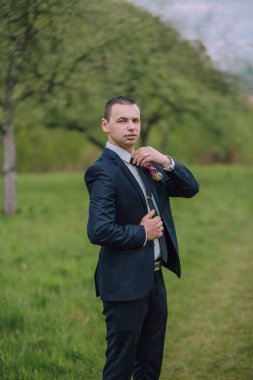 Takım elbiseli bir adam elinde pembe bir çiçekle bir tarlada duruyor. Kravat takıyor ve resmi bir etkinliğe hazırlanıyor.