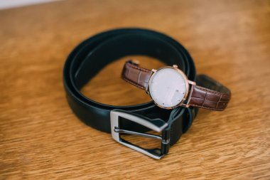 Tahta bir masanın üzerine bir saat ve bir kemer yerleştirilir. Bu saat altın ve siyah.