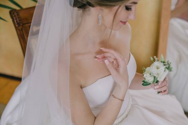 Kafasında beyaz bir peçe ve elinde bir çiçekle bir sandalyede oturan bir gelin.