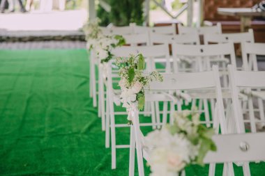 Üzerinde çiçekler olan beyaz sandalyeler yeşil bir halının üzerinde düzenlenir. Sandalyeler sıralanır, bazıları kameraya bakar, diğerleri de uzağa bakar.