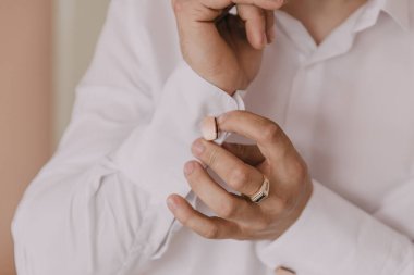 Bir adam resmi bir olaya hazırlanıyor ve altın bir yüzük ve kol düğmesi takıyor.