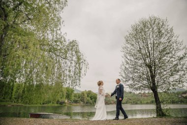 Bir gelin ve damat bulutlu bir günde gölün kenarında yürüyorlar. Gelin beyaz bir elbise giyiyor ve damat mavi bir takım elbise giyiyor. Sahne huzurlu ve romantik.