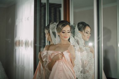 Bir kadın düğün için hazırlanıyor ve elbisesini düzeltiyor. Kadının güzel pembe bir elbise giydiği ve aynanın önünde durduğu için, görüntüde romantik ve zarif bir hava var.