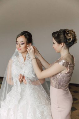 Bir gelin saçını ve makyajını bir kadına yaptırıyor. Gelin beyaz bir elbise giyiyor ve kadın pembe bir elbise giyiyor.