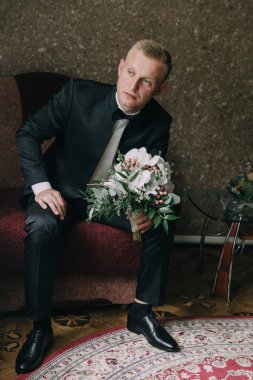 Takım elbiseli bir adam kırmızı bir sandalyede elinde bir buket çiçekle oturuyor. Zarafet ve entelektüellik kavramı. Çünkü adam takım elbise ve kravat takmış.