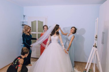 Bir gelin nedimeleriyle düğününe hazırlanıyor. Gelin beyaz bir elbise giyiyor ve nedimeler duvağı için ona yardım ediyorlar. Sahne neşeli ve kutlayıcıdır.