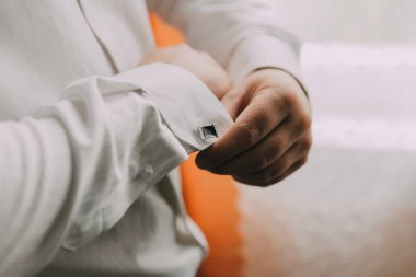 Bir adam giyiniyor ve kol düğmelerini ayarlıyor. Formalite ve detaylara dikkat etme kavramı. Adam kıyafetini dikkatlice hazırlıyor.