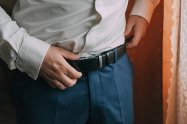 Bir adam mavi kemer ve gömlek giyiyor. Kemerini ayarlıyor.