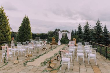 Güzel bir açık havada düğün töreni düzenleniyor. Tören, beyaz kemerli ve uzun beyaz koridorlu geniş bir açık alanda gerçekleşecek. Sandalyeler sıraya dizildi.