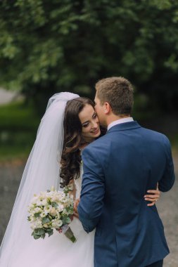 Gelin ve damat birbirlerine sarılıyorlar, gelin de bir buket çiçek tutuyor. Sahne aşk ve mutluluktur. Çiftler düğün günlerini kutluyorlar.