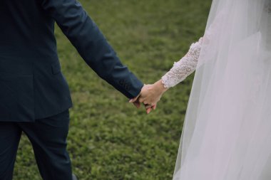 Bir gelin ve damat çimen tarlasında el ele tutuşuyorlar. Gelin beyaz bir elbise giyiyor ve damat mavi bir takım elbise giyiyor. Sahne huzurlu ve romantik, aşkı yakalıyor.