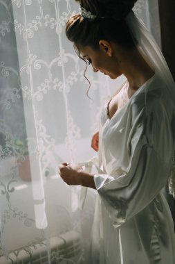 Beyaz elbiseli bir kadın pencerenin önünde dikiliyor ve dünyaya bakıyor.