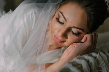 Bir gelin elleri yüzü üzerinde bir yatakta uzanıyor. Beyaz bir elbise ve duvak takıyor.