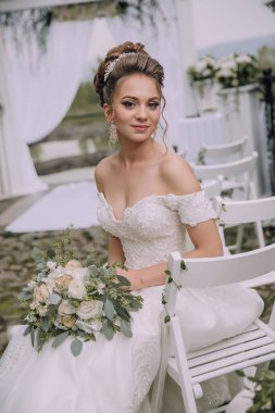 Güzel bir gelin kucağında bir buket çiçekle beyaz bir sandalyede oturur. Beyaz bir elbise giyiyor ve saçları zarif bir topuz şeklinde. Sahne bir bahçede ya da dışarıda geçiyor.