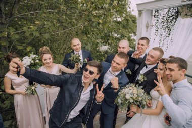 Bir grup insan fotoğraf için poz veriyor, bir adam cep telefonuyla selfie çekiyor.