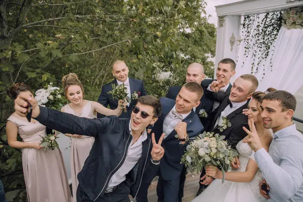 Bir grup insan fotoğraf için poz veriyor, bir adam cep telefonuyla selfie çekiyor.