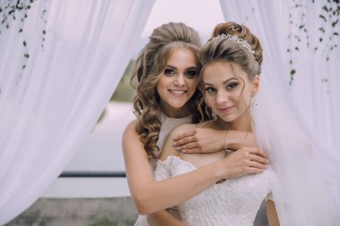 İki kadın fotoğraf için poz veriyor, biri gelinlik giyiyor. Sahne mutlu ve kutlama dolu.