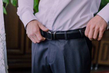 Bir adam siyah kuşak takıyor ve ayarlıyor. Görüntünün rahat ve rahat bir havası var.