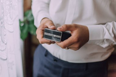 Bir adam elinde küçük bir kara kutu tutuyor. Kutu muhtemelen bir hediye ya da minnettarlık göstergesi. Adamın ifadesi ciddi ve odaklanmış. Bu da kutuyu dikkatle tuttuğunu gösteriyor.