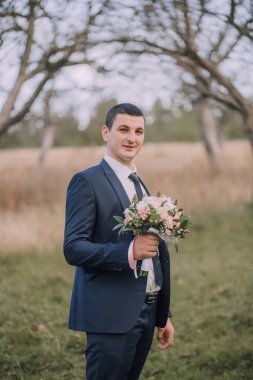 Elinde bir buket çiçek tutan takım elbiseli bir adam. Zarafet ve incelik kavramı, erkek takım elbise ve kravat giyer, ve çiçekler sahneye doğal bir güzellik katar