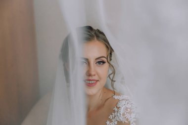 Bir gelin perdenin önünde duruyor, yüzü kısmen gizlenmiş. Beyaz bir elbise ve duvak takıyor. Gizem ve beklenti kavramı