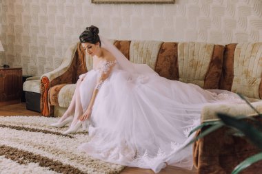 Gelinlikli bir kadın kanepede oturuyor. Beyaz bir elbise ve duvak takıyor.