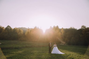 Bir gelin ve damat güneş üzerlerine doğarken bir tarlada dururlar. Sahne huzurlu ve huzurlu, çift mutlu ve mutlu görünüyor.