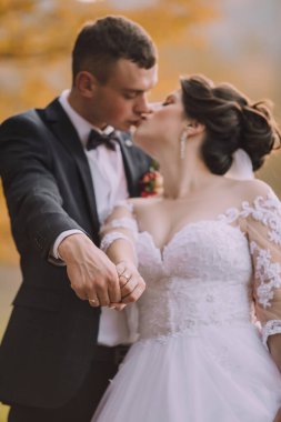 Bir gelin ve damat birbirlerinin ellerini öpüyor. Gelin beyaz bir elbise giyiyor ve damat siyah bir takım giyiyor.