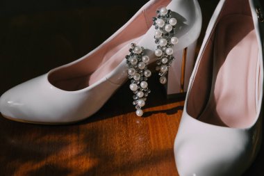 Ayak ve topuğunda inci olan beyaz bir çift ayakkabı. Ayakkabılar ahşap bir yüzeye yerleştirilir.