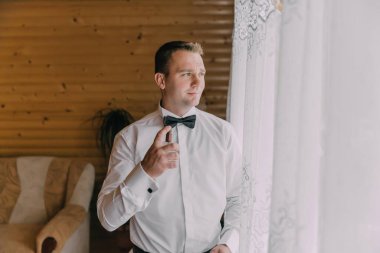 Takım elbiseli ve kravatlı bir adam dışarı çıkmaya hazırlanıyor. Kravatını takıyor ve parfüm sıkıyor.