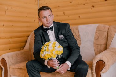 Takım elbiseli ve kravatlı bir adam elinde bir buket sarı çiçekle kanepede oturur. Zarafet ve entelektüellik anlayışı, çünkü adam resmi giyinmiş.