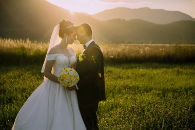 Bir gelin ve damat güneş üzerlerine doğarken bir tarlada dikiliyorlar. Gelin beyaz bir elbise giyiyor ve damat siyah bir takım elbise giyiyor. El ele tutuşup birbirlerine bakıyorlar.