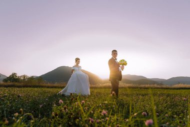 Bir gelin ve damat çiçek tarlasında durur. Gelin beyaz bir elbise giyiyor ve damat bir takım elbise giyiyor. Güneş ışıl ışıl parlıyor, sahne üzerine sıcak bir parıltı saçıyor.