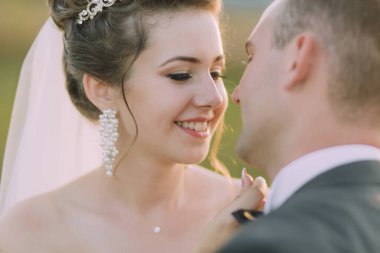 Gelin ve damat birbirlerini kucaklıyor, gelin beyaz bir elbise giyiyor ve damat takım elbise giyiyor.