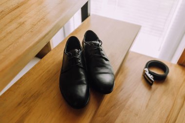 Ahşap bir masada iki siyah ayakkabı var. Ayakkabılar pencerenin önündeki masaya konur.