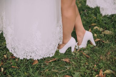 Bir gelin ve kızı çim tarlasında duruyorlar. Gelin beyaz bir elbise giyiyor ve kızı beyaz ayakkabılar giyiyor. Sahne huzurlu ve sakin, çimlerle