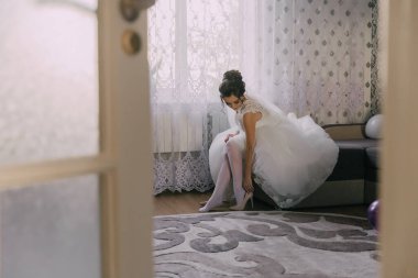 Gelinlik giymiş bir kadın düğüne hazırlanıyor. Beyaz elbisesini giyiyor ve ayakkabılarını tamir ediyor.