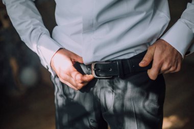 Bir adam siyah kuşak takıyor ve onu ayarlıyor. Görüntünün rahat ve rahat bir havası var, çünkü adam kemerini ayarlıyor ve acelesi yok.