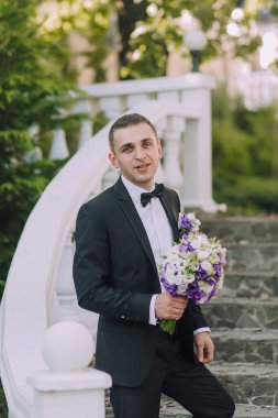 Siyah takım elbiseli ve papyonlu bir adam elinde bir buket çiçek tutuyor. Zarafet ve entelektüellik anlayışı, çünkü adam resmi giyinmiş.