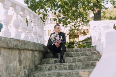 Takım elbise giyen ve elinde bir buket çiçek tutan bir adam merdivenlerde oturuyor.