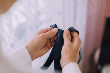 Bir adam siyah bir kravat tutuyor ve ayarlıyor. Formalite kavramı ve detaylara dikkat, çünkü adam kravatın düzgün ve düzgün görünmesini sağlamak için dikkatlice ayarlıyor.