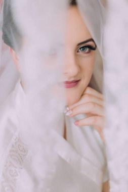 Beyaz bir elbise giyen ve saçları topuz şeklinde olan bir kadın. O bir peçe takıyor ve elleri yüzünde.