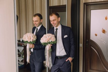 Takım elbiseli bir adam aynanın önünde bir buket çiçek tutuyor. Zarafet ve entelektüellik kavramı. Çünkü adam takım elbise ve kravat takmış.