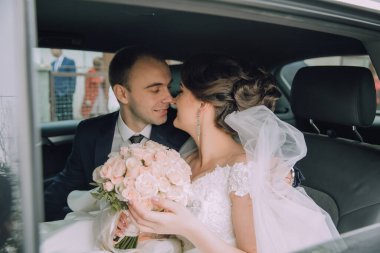 Gelin ve damat arabada, gelin elinde buket tutuyor. Sahne romantik ve mutlu.