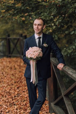 Elinde bir buket çiçek tutan takım elbiseli bir adam. Adam gülümsüyor ve mutlu.