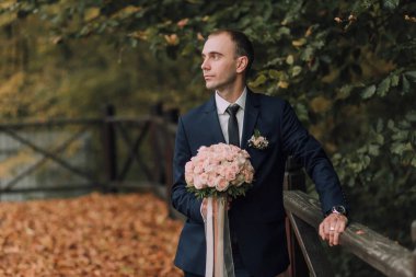 Elinde bir buket çiçek tutan takım elbiseli ve kravatlı bir adam. Adam ahşap bir çitin üzerinde duruyor, kameraya bakıyor. Zarafet ve entelektüellik anlayışı, çünkü adam resmi giyinmiş.