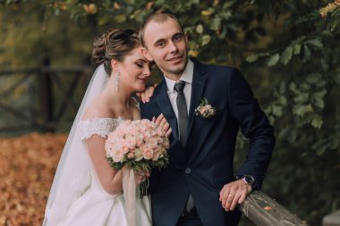 Bir gelin ve damat bir buket ve kravat ile bir resim için poz veriyorlar. Gelin beyaz bir elbise giyiyor ve damat mavi bir takım elbise giyiyor. Sahne mutlu ve kutlama dolu.