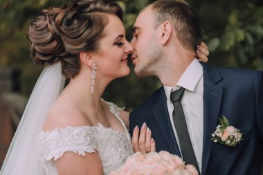 Gelin ve damat ormanda öpüşürler. Gelin beyaz bir elbise giyiyor ve damat mavi bir takım giyiyor.